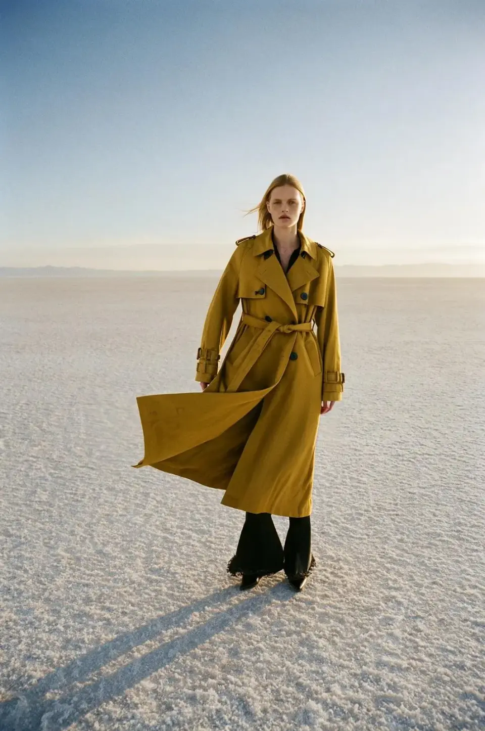 A model in a mustard trench coat on a salt flat